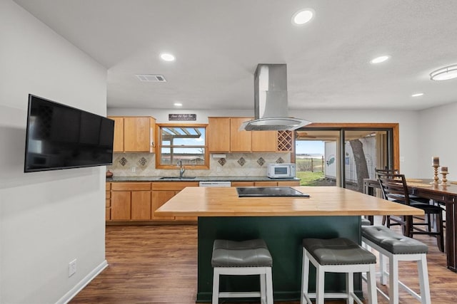 kitchen featuring white microwave, visible vents, island exhaust hood, wood counters, and a sink