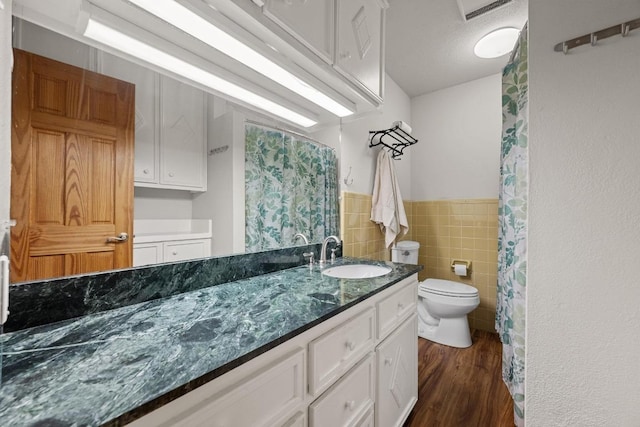 bathroom with toilet, wood finished floors, tile walls, wainscoting, and vanity