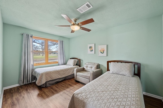 bedroom with visible vents, baseboards, a textured ceiling, and wood finished floors