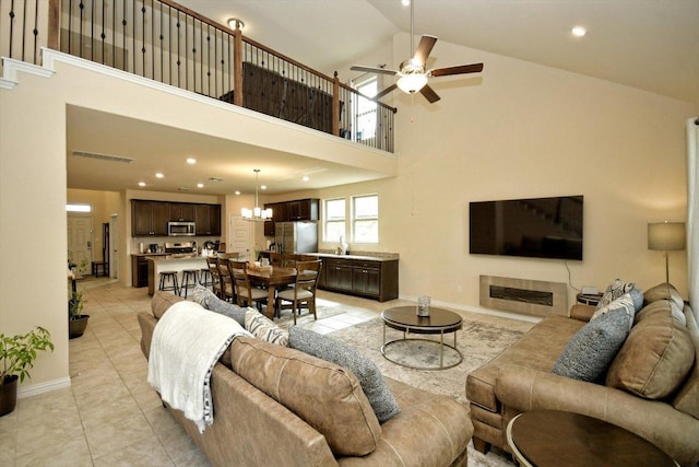 living area with visible vents, baseboards, high vaulted ceiling, and ceiling fan with notable chandelier