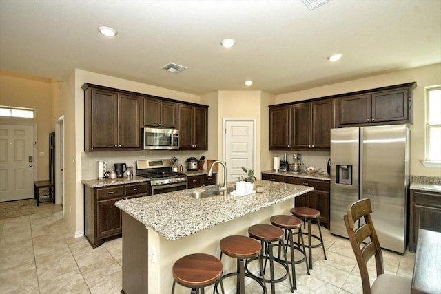 kitchen featuring a sink, stainless steel appliances, a kitchen bar, and dark brown cabinets