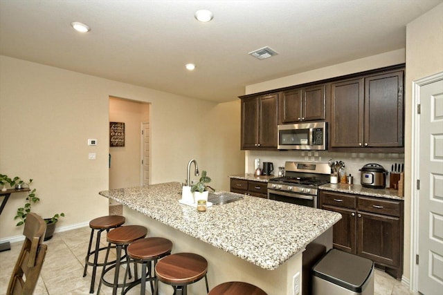 kitchen featuring visible vents, a kitchen island with sink, a sink, appliances with stainless steel finishes, and a kitchen bar