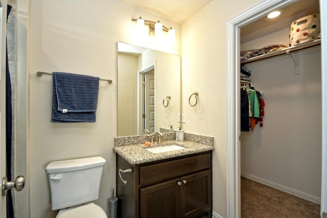 bathroom with a spacious closet, toilet, vanity, and baseboards