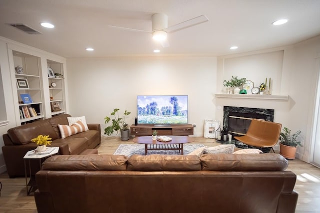 living room featuring recessed lighting, visible vents, built in features, and a premium fireplace