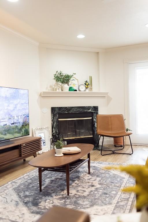 living area with a high end fireplace, ornamental molding, and wood finished floors