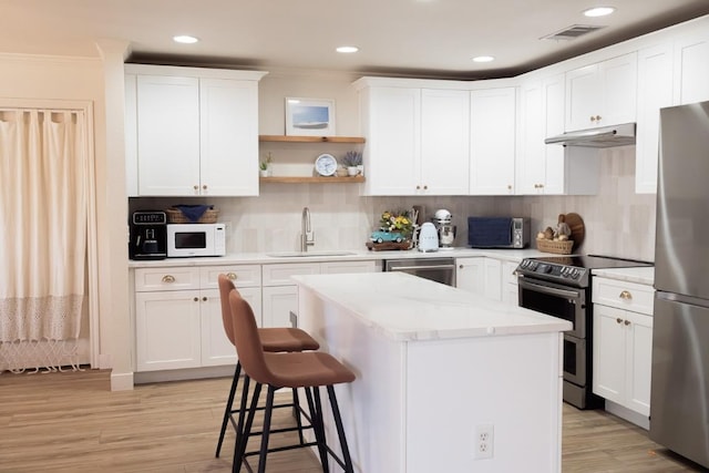 kitchen with visible vents, a sink, under cabinet range hood, a center island, and appliances with stainless steel finishes