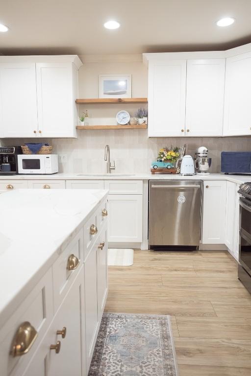 kitchen with a sink, decorative backsplash, appliances with stainless steel finishes, white cabinetry, and light wood-type flooring