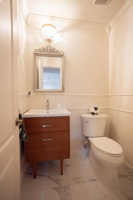 half bath with vanity, crown molding, toilet, and marble finish floor