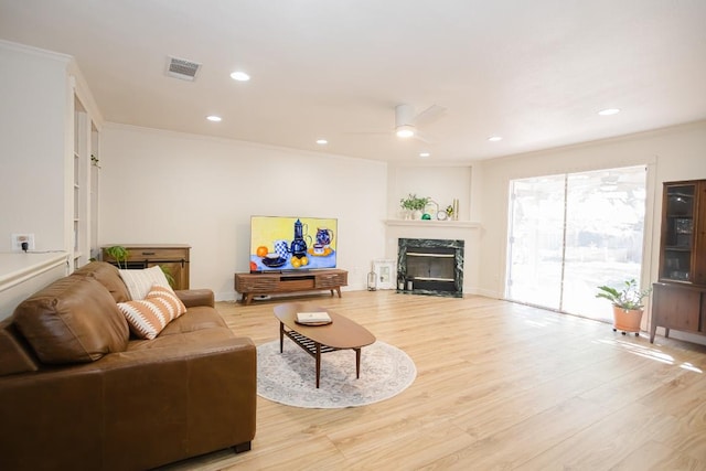 living room with ornamental molding, ceiling fan, light wood-style flooring, a premium fireplace, and recessed lighting