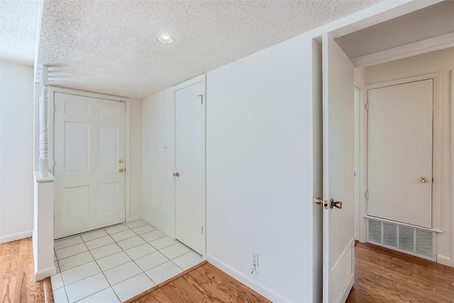 entryway with visible vents, a textured ceiling, light wood-type flooring, and baseboards