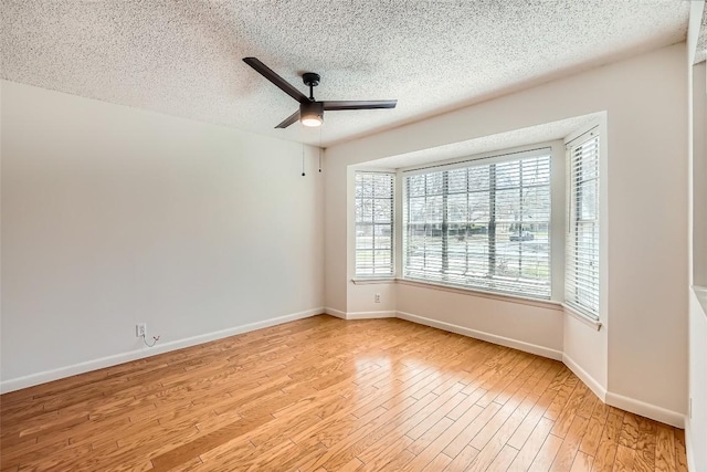 spare room with a textured ceiling, baseboards, light wood-type flooring, and a ceiling fan