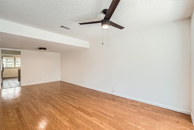 spare room featuring visible vents, a textured ceiling, light wood finished floors, baseboards, and ceiling fan