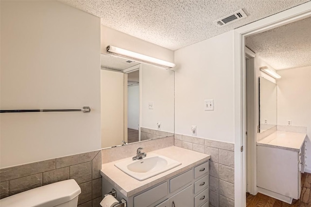 bathroom featuring visible vents, toilet, a textured ceiling, tile walls, and vanity