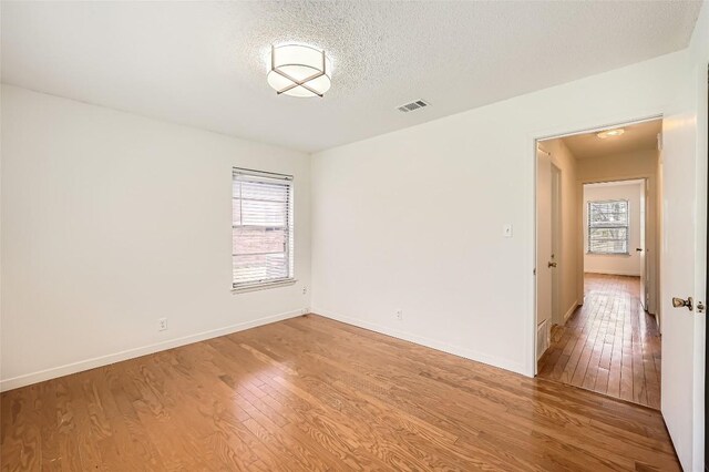 spare room featuring plenty of natural light, light wood-style floors, visible vents, and a textured ceiling