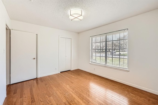 unfurnished bedroom featuring light wood finished floors, a closet, a textured ceiling, and baseboards