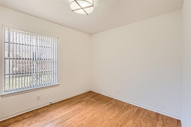 empty room with baseboards, a textured ceiling, and light wood-style floors