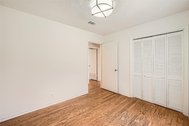 unfurnished bedroom featuring visible vents, baseboards, light wood-style floors, a closet, and a textured ceiling