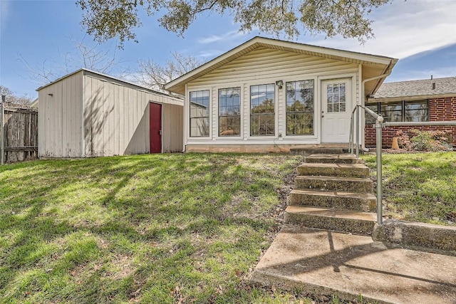 rear view of property with a storage shed, an outbuilding, a yard, and fence