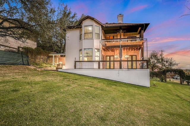 rear view of property with stucco siding, a patio, a yard, a balcony, and a chimney