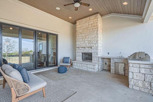 view of patio / terrace featuring ceiling fan, an outdoor stone fireplace, an outdoor kitchen, a grill, and a sink