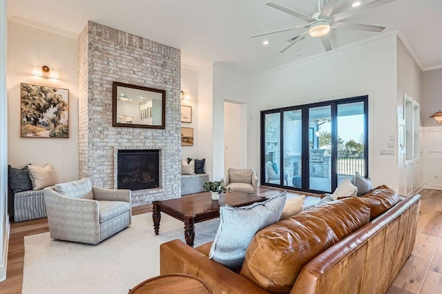 living area featuring light wood-type flooring, a brick fireplace, ornamental molding, and a ceiling fan