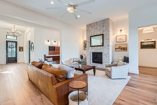 living area with baseboards, light wood-style flooring, a fireplace, crown molding, and ceiling fan with notable chandelier