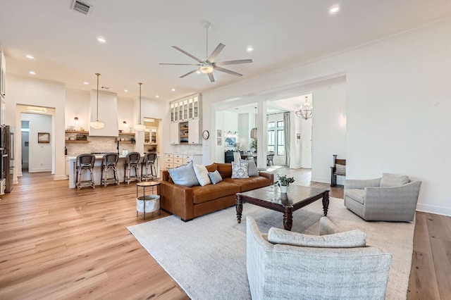 living room with visible vents, recessed lighting, ornamental molding, light wood-style floors, and ceiling fan with notable chandelier