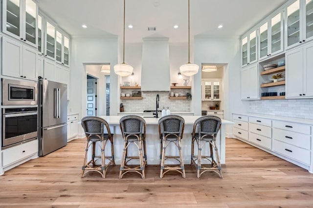 kitchen with a breakfast bar area, open shelves, stainless steel appliances, custom range hood, and light wood-type flooring