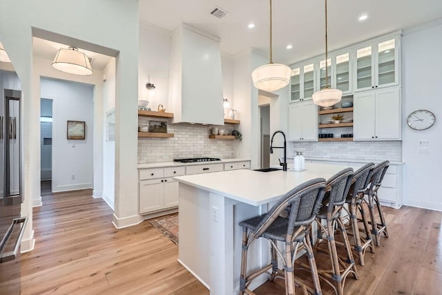 kitchen featuring visible vents, open shelves, light countertops, light wood-style flooring, and a sink