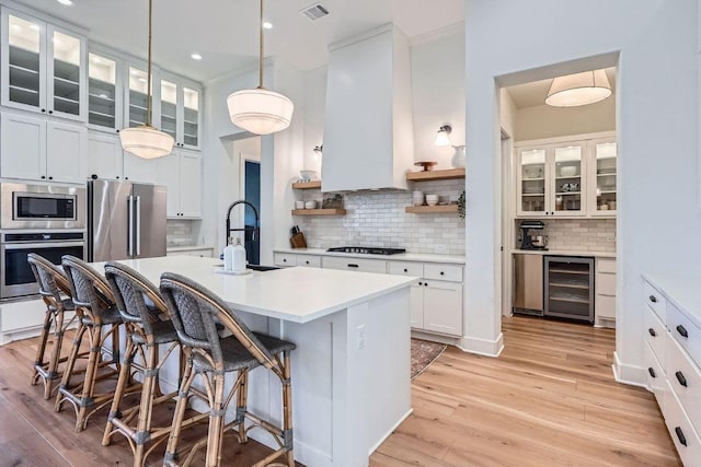 kitchen featuring premium range hood, a sink, wine cooler, light wood-style floors, and appliances with stainless steel finishes