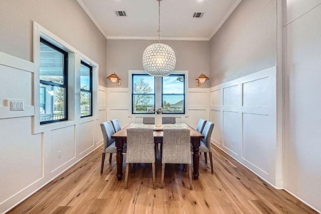 dining area with a decorative wall, light wood-style flooring, visible vents, and a chandelier