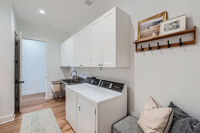 laundry area with washing machine and clothes dryer, visible vents, light wood finished floors, cabinet space, and a sink