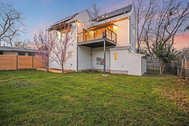 back of property at dusk featuring a yard, a balcony, and a fenced backyard