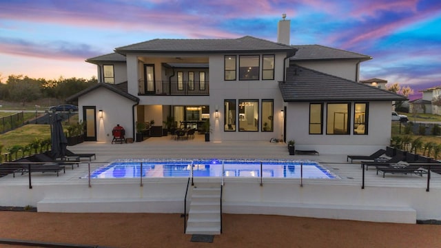 rear view of house with a patio, a balcony, a chimney, stucco siding, and a tile roof