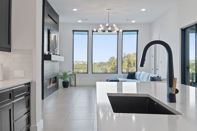 kitchen with light tile patterned flooring, a tile fireplace, a sink, light countertops, and tasteful backsplash