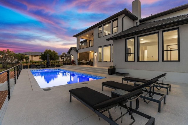 pool at dusk with a fenced in pool and a patio