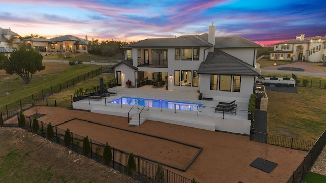 back of property at dusk with a tile roof, fence, a balcony, a chimney, and a patio area