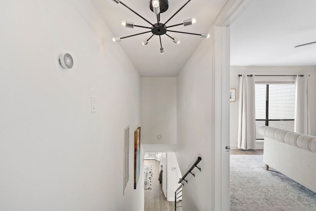 hall with an upstairs landing, an inviting chandelier, and wood finished floors