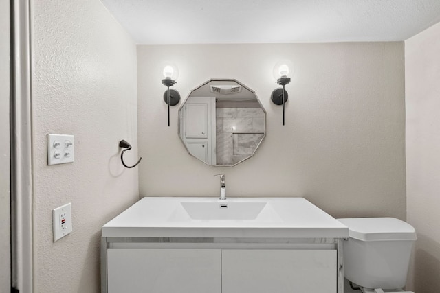 bathroom with vanity, toilet, and a textured wall