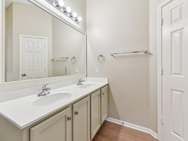 bathroom featuring double vanity, wood finished floors, baseboards, and a sink