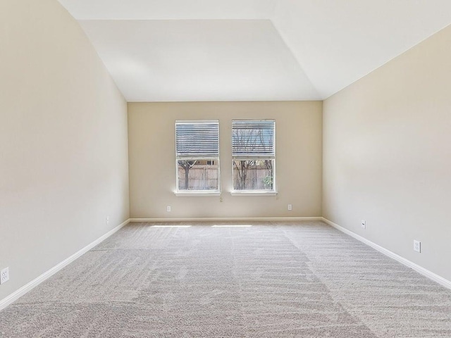 carpeted empty room featuring baseboards and vaulted ceiling