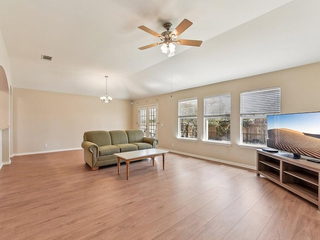 living area featuring visible vents, light wood-style flooring, ceiling fan with notable chandelier, baseboards, and lofted ceiling