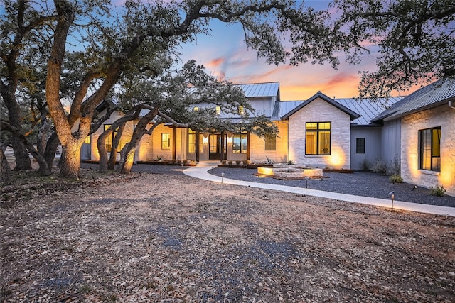 back of property at dusk with stone siding, metal roof, a standing seam roof, and an outdoor fire pit