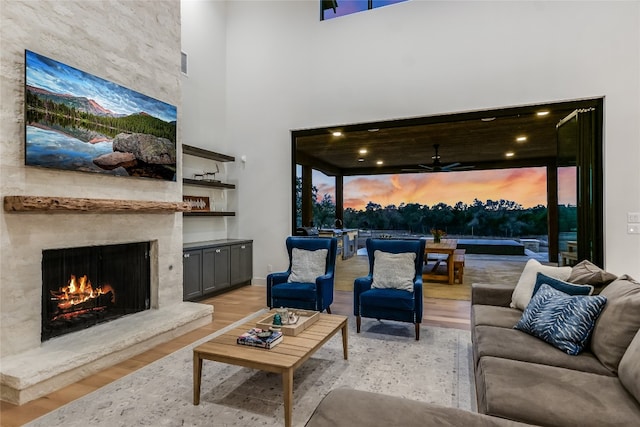 living room featuring baseboards, light wood-type flooring, a fireplace, a high ceiling, and a ceiling fan