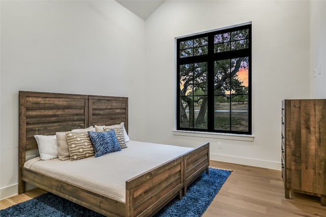 bedroom featuring baseboards, lofted ceiling, and light wood finished floors