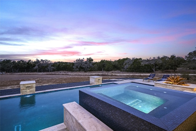 pool at dusk with an in ground hot tub