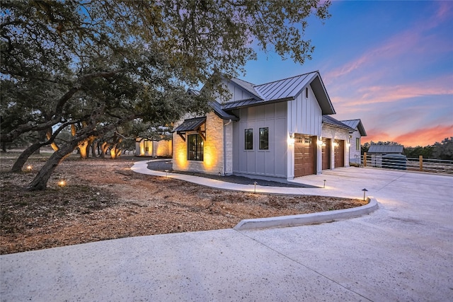 property exterior at dusk featuring board and batten siding, fence, metal roof, a garage, and a standing seam roof