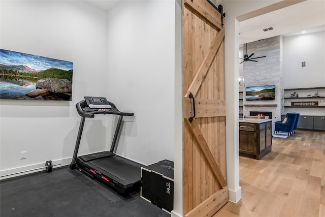 exercise room featuring visible vents, a barn door, a large fireplace, light wood-style floors, and baseboards