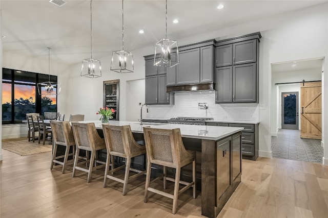 kitchen featuring light wood-type flooring, a kitchen island with sink, gray cabinets, a barn door, and tasteful backsplash