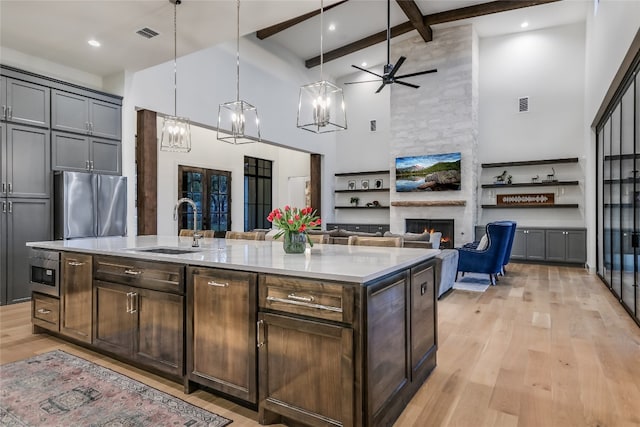 kitchen with light wood-type flooring, beamed ceiling, a sink, freestanding refrigerator, and light countertops